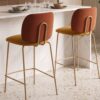 Taburetes Lora con respaldo teja, asiento mostaza y patas metálicas claras junto a una isla